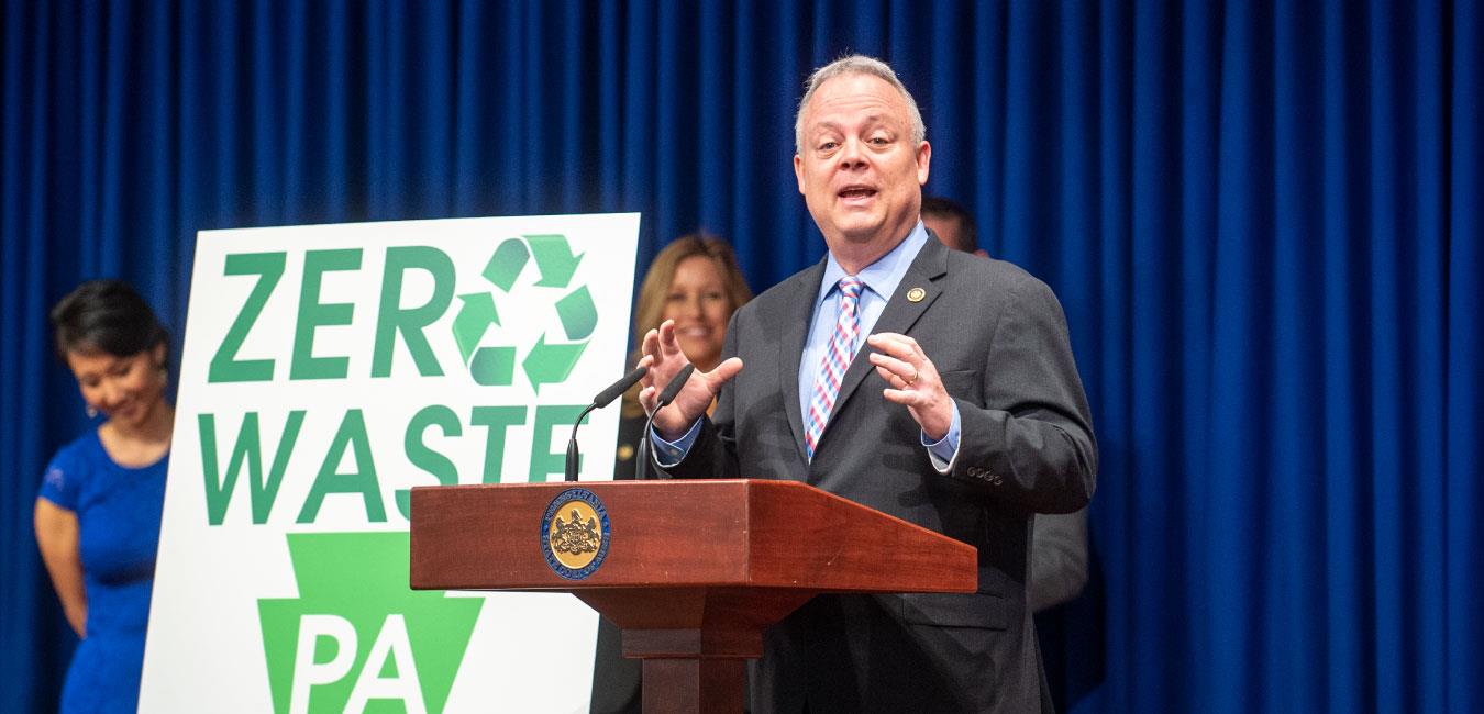 Representative Warren holding both hands up and speaking at podium at Zero Waste event in Capitol Media Center