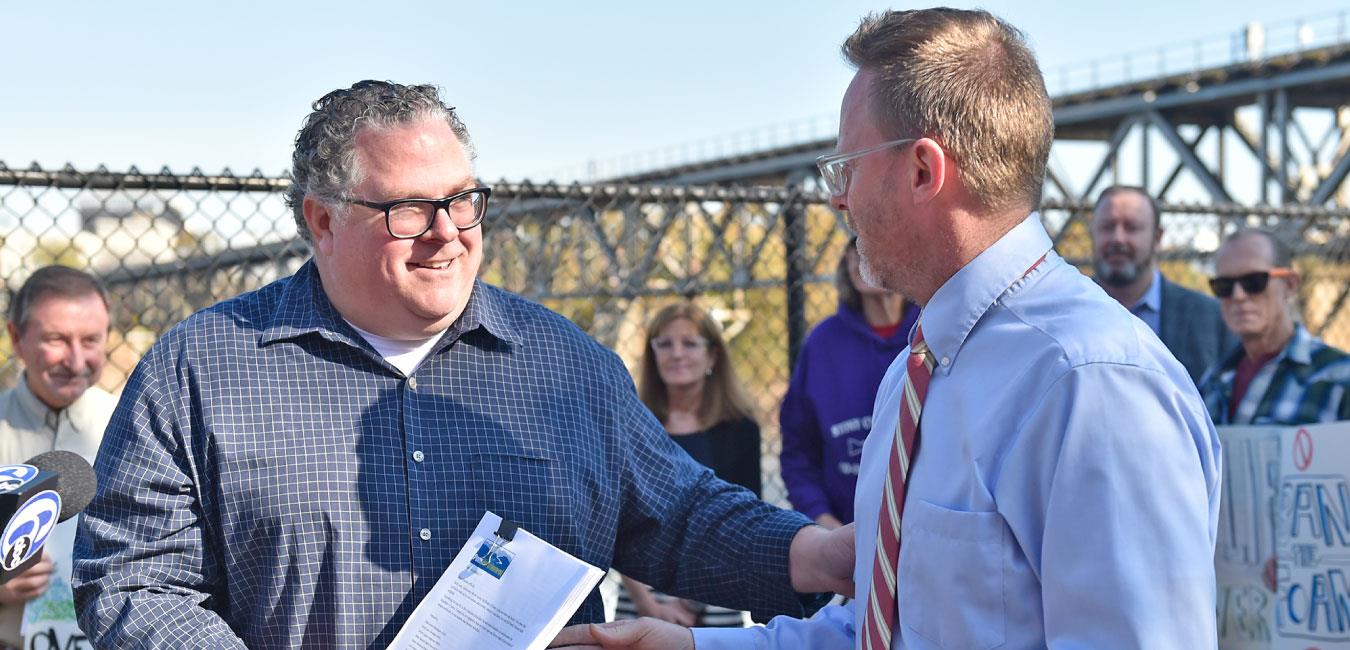 Representative Briggs holding papers, smiling, and speaking to man at outdoor event